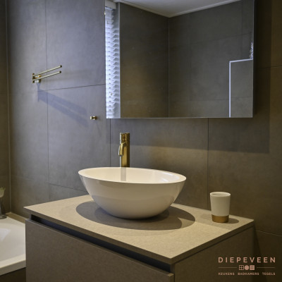 Spiegel met ledverlichting en een egale witte wasbak gecombineerd met een goudlook kraan