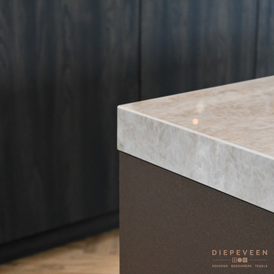 In de keuken is er gewerkt met natuurlijke elementen en kleuren. Het Dekton werkblad is met zijn 80mm dikte een echte eyecatcher. De aders van het werkblad sluiten aan bij het bronzen front van het eiland. De donker houten fronten van de kastenwand hebben een sjieken uitstraling. Kortom een warme en sfeervolle match