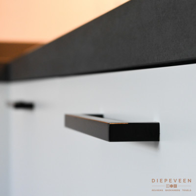 Het donkergrijze rustieke werkblad is in  contrast met de matte witte fronten. Ook de zwarte stijlvolle greep past helemaal thuis in deze combinatie